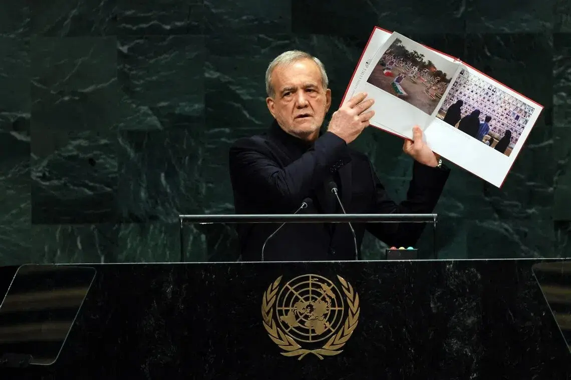 Iranian President Masoud Pezeshkian holds up pictures of alleged victims killed during the Israeli and American air strikes