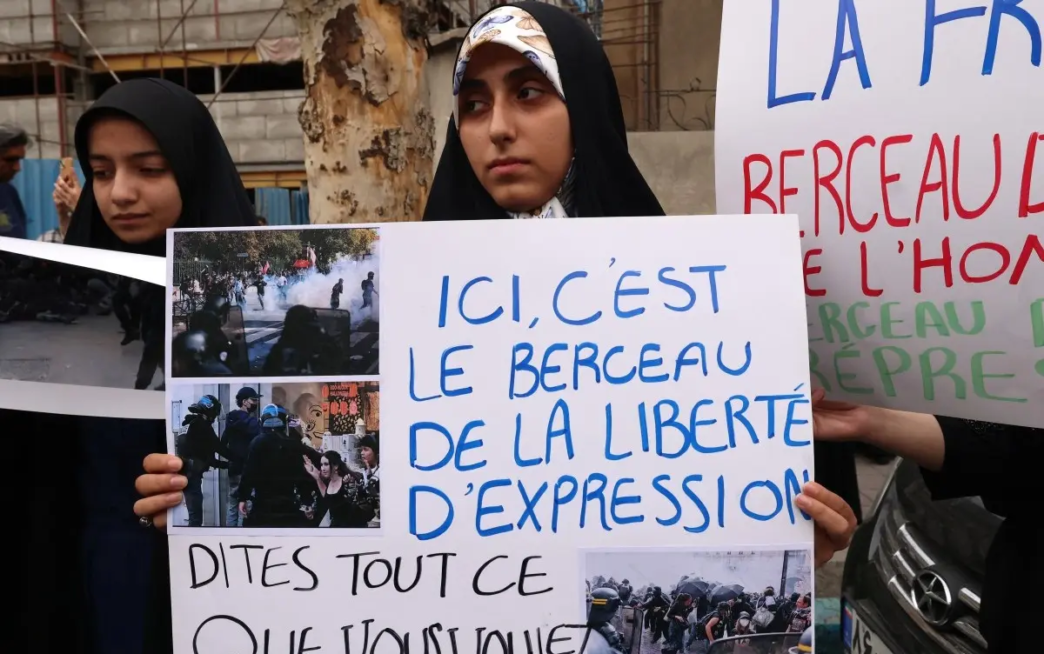 Iranian citizens and students hold signs with images as they gather outside the French Embassy to protest the French police action during nationwide French student protests, in Tehran on October 10, 2026.