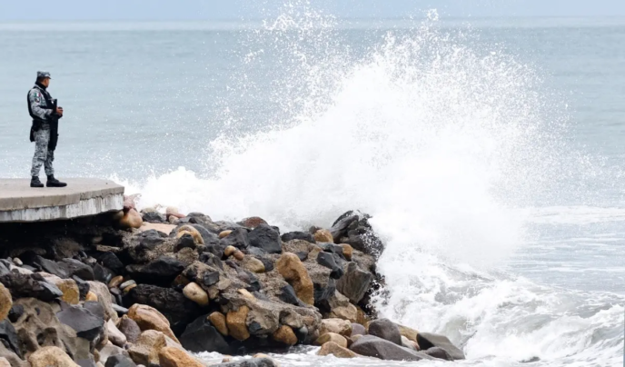 A member of Mexico's National Guard stands on the Puerto Vallarta boardwalk as waves crash against the shoreline ahead of the potential impact of Hurricane Simon in Puerto Vallarta, Jalisco state, Mexico, on October 11, 2026.