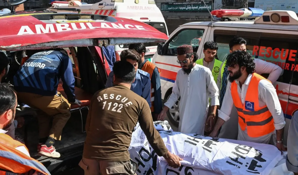 Volunteers and relatives shift the body of a victim, killed after a roof collapsed at a school, into an ambulance outside a hospital in Peshawar on October 15, 2026.