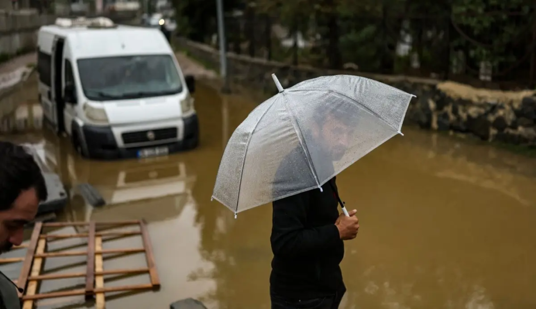 A man holds his umbrella next to vehicle submerged by floodewaters following heavy rain at Ayazaga district in Istanbul on October 15, 2026.