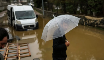 A man holds his umbrella next to vehicle submerged by floodewaters following heavy rain at Ayazaga district in Istanbul on October 15, 2026.