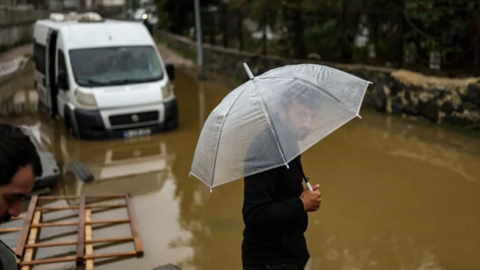 A man holds his umbrella next to vehicle submerged by floodewaters following heavy rain at Ayazaga district in Istanbul on October 15, 2026.