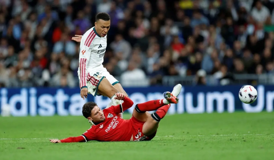 Real Madrid's French forward #10 Kylian Mbappe fights for the ball with Sevilla's Spanish defender #22 Jose Angel Carmona (down) during the Spanish league football match between Real Madrid CF and Sevilla FC at the Santiago Bernabeu stadium in Madrid on October 18, 2026.