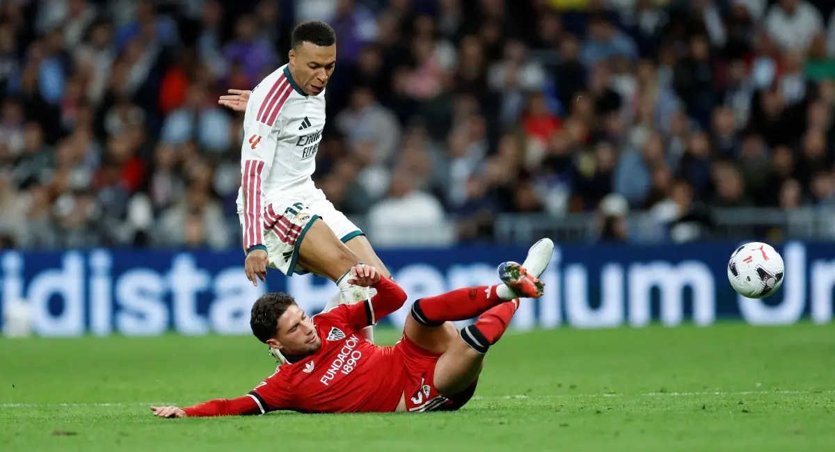 Real Madrid's French forward #10 Kylian Mbappe fights for the ball with Sevilla's Spanish defender #22 Jose Angel Carmona (down) during the Spanish league football match between Real Madrid CF and Sevilla FC at the Santiago Bernabeu stadium in Madrid on October 18, 2026.